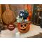 A handcrafted gourd character. It has a carved face and a custome jean hat. It's name is Ripple. A battery-operated candle is included